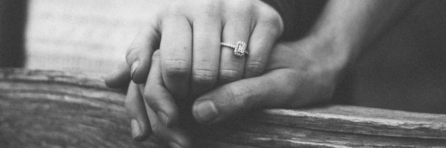 black and white photo of woman and man holding hands with engagement ring on woman's ring finger