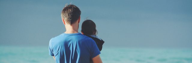 dad holding daughter at the beach