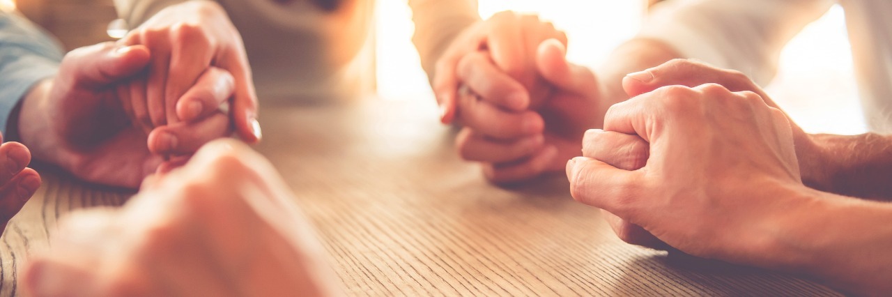 How Grief Can Resurface With a Second Loved One Facing Cancer Cropped image of people holding hands while sitting around a table. Only hands are in the frame.
