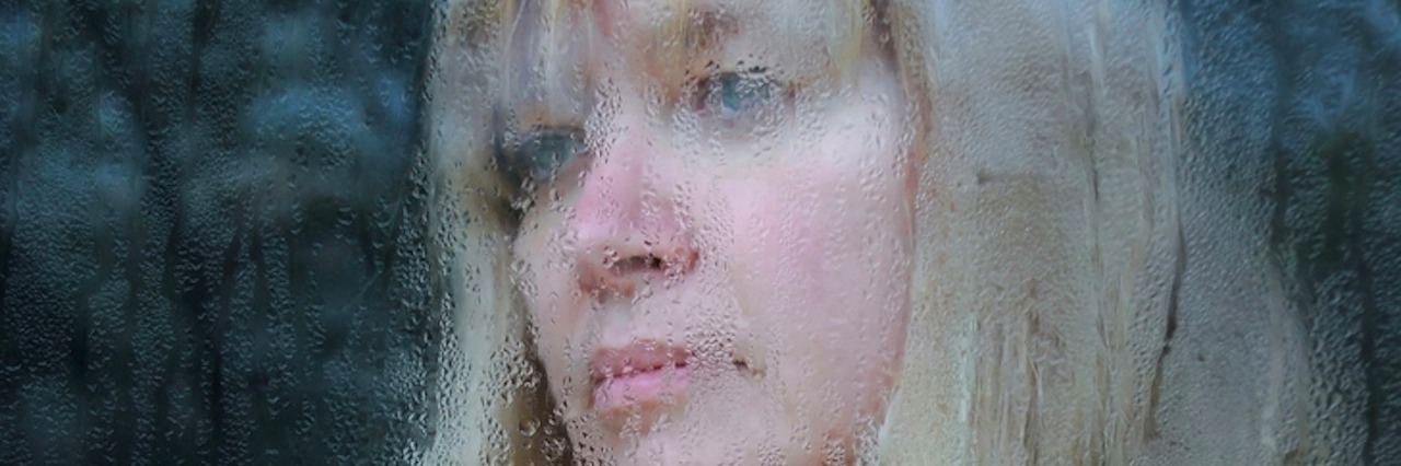 Harm OCD Makes Me Feel Like a Violent Person Sometimes Portrait of the middle-aged woman looking through the window on a rainy day