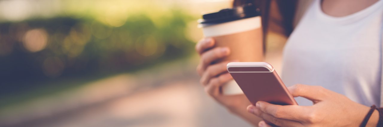 Close-up image of woman texting and drinking coffee outdoors