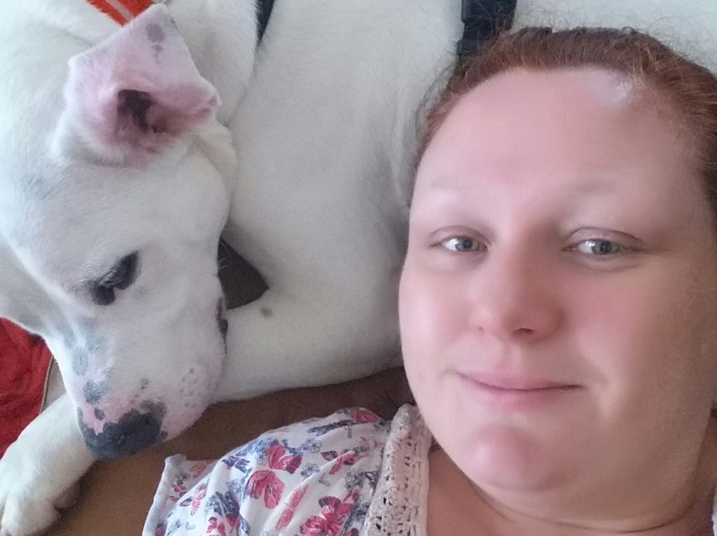 woman lying down with white american bulldog lying beside her with head resting on paw