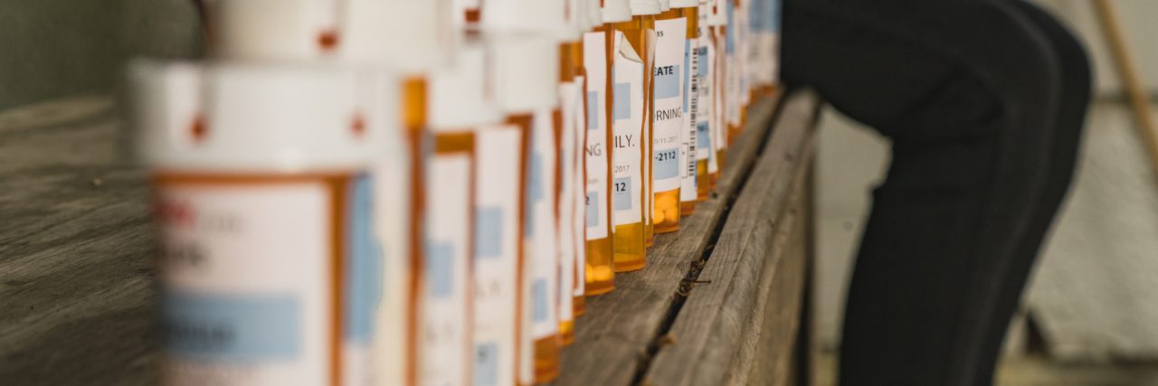 Quiz: How Much Do You Know About Mental Health Medications? woman on bench with a line of many medication bottles
