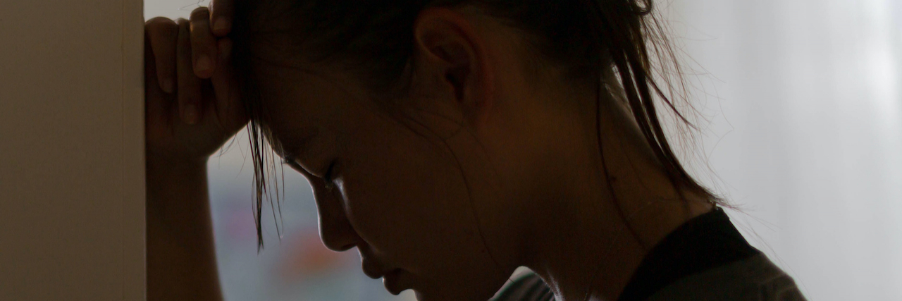 Woman leaning against a wall with her head down