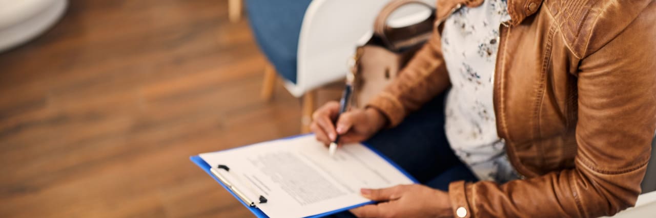 15 Secrets of People Who Can't Work Because of an Illness woman with face mask filling out medical papers in a waiting room.