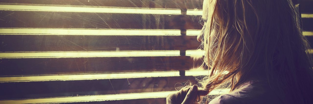 blonde woman looking through blinds into sunlight anxious upset