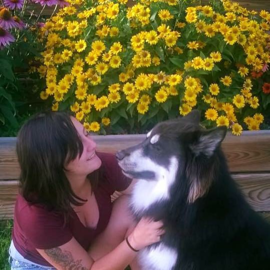 woman and black and white alaskan malamute sitting in front of flowers