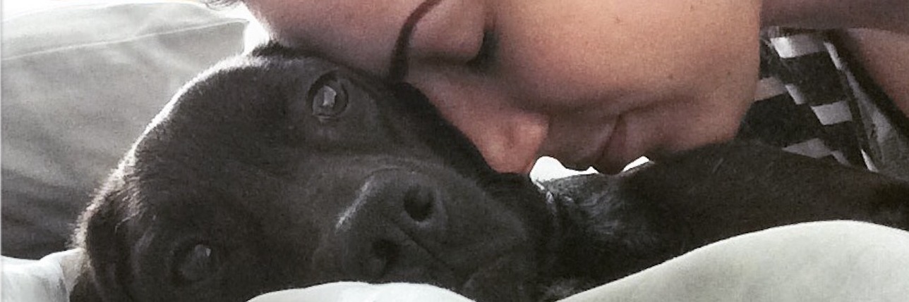 How My Dog Helps My Anxiety and Panic Attacks image of young woman resting head lovingly on black labrador dog