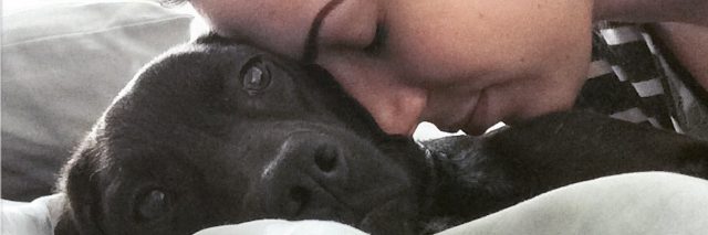 image of young woman resting head lovingly on black labrador dog