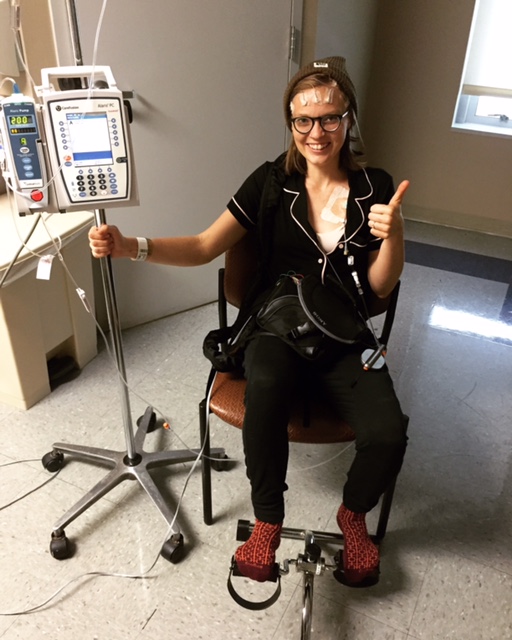 aubrey winkie sitting in chair at doctor's office next to iv giving thumbs up