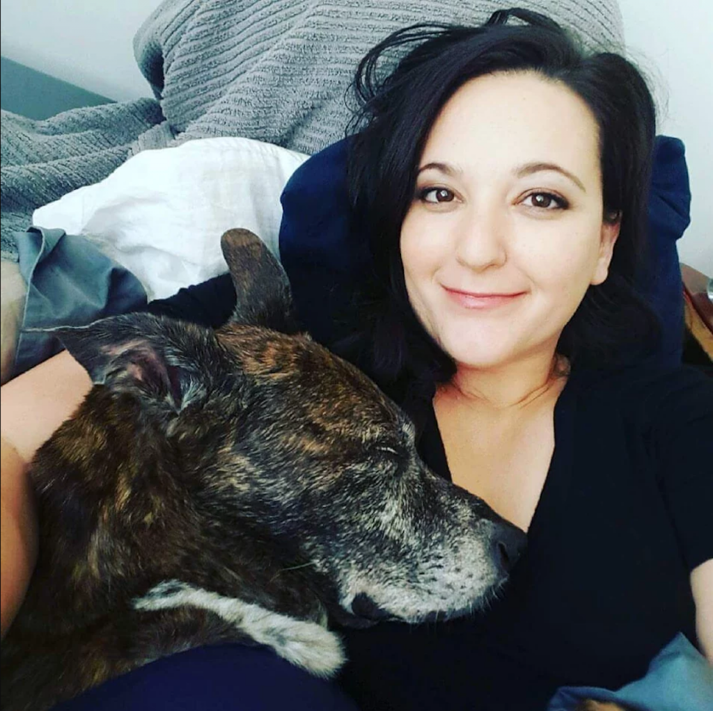 woman smiling and lying in bed with her dog