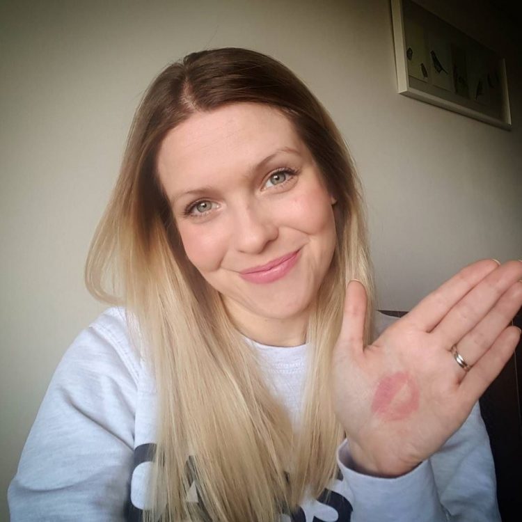 Woman holding her hand up to the camera, with a lipstck kiss on her hand.