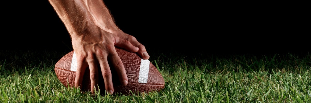 Why I Compare Life With Multiple Sclerosis to a Sports Game Hands on football in grass.