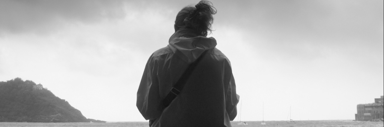 Defining and Understanding Grief: My Experience Woman sitting on front of the sea on an overcast day