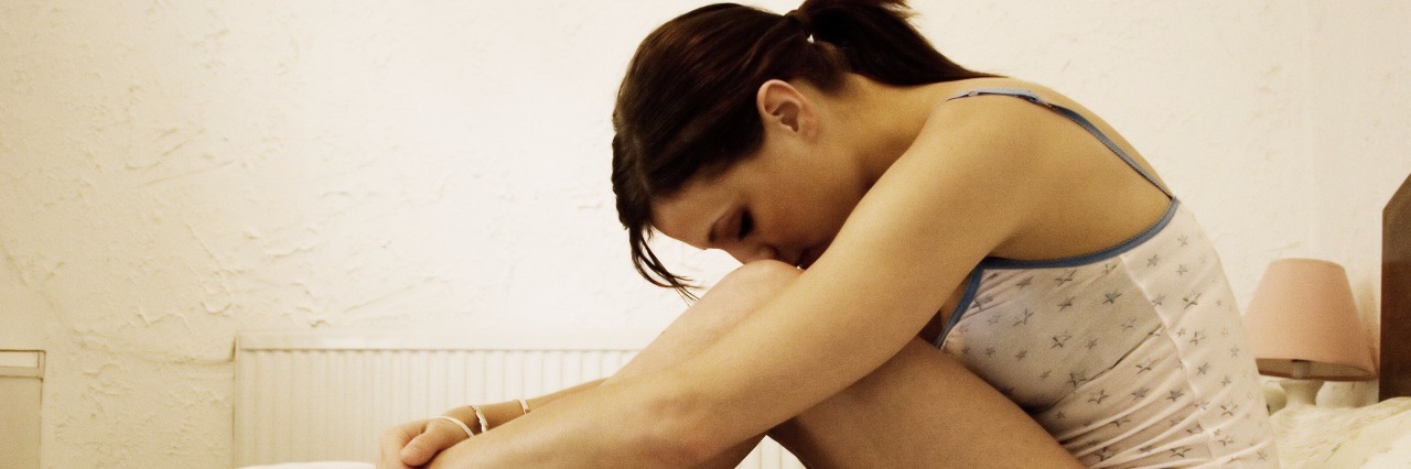 When Anxiety Makes Me Insecure About Everything young woman sat on bed hugging knees upset