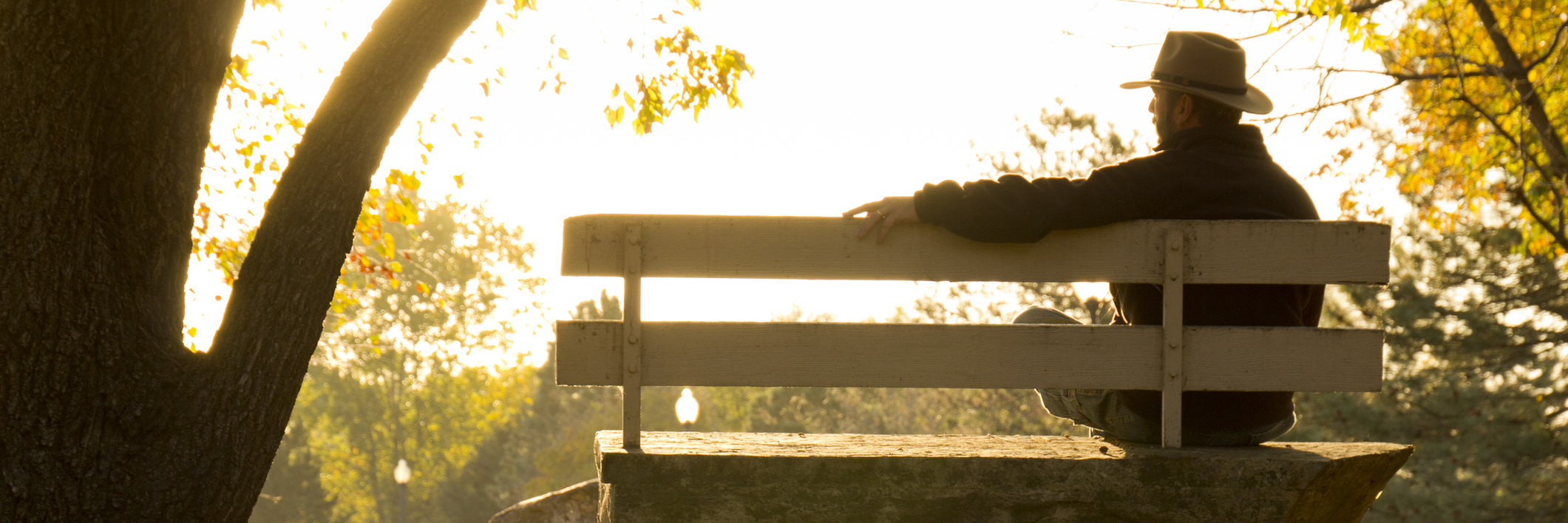Redefining What It Means to Be a Cancer Survivor man sitting on a park bench at sunrise