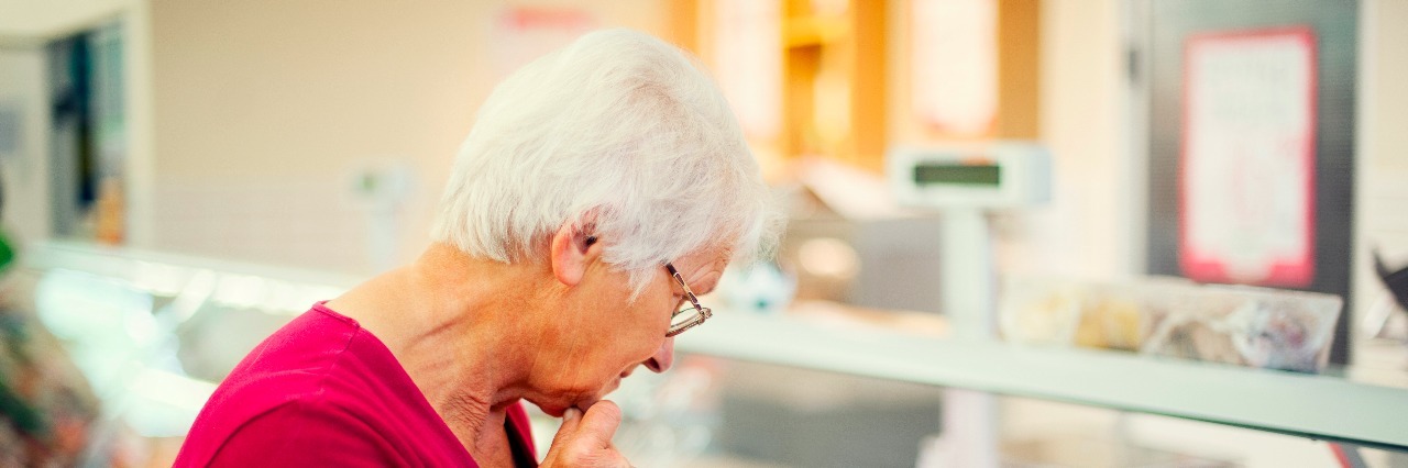 Elderly woman in red shirt examining cheeses at a market