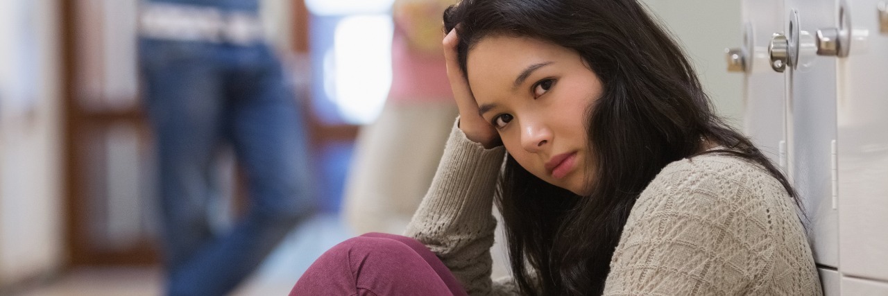 When You Want to Speak About Suicidal Thoughts but Afraid of Stigma sad student sitting on floor next to lockers and red backpack