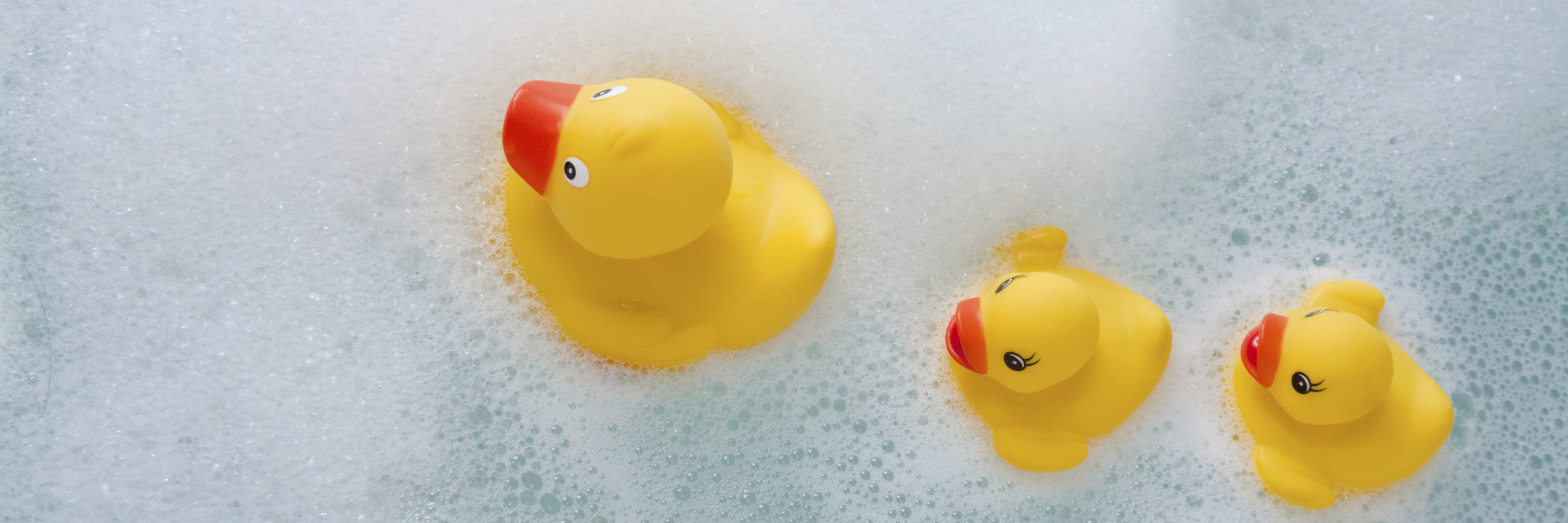 3 rubber ducks of different sizes floating in soapy bath water