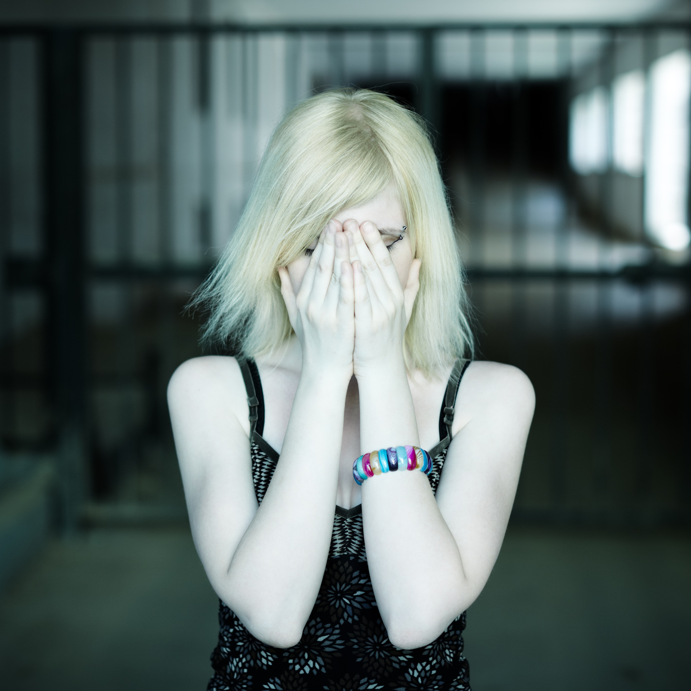 woman in dark hallway with hands covering face and eyes looking upset