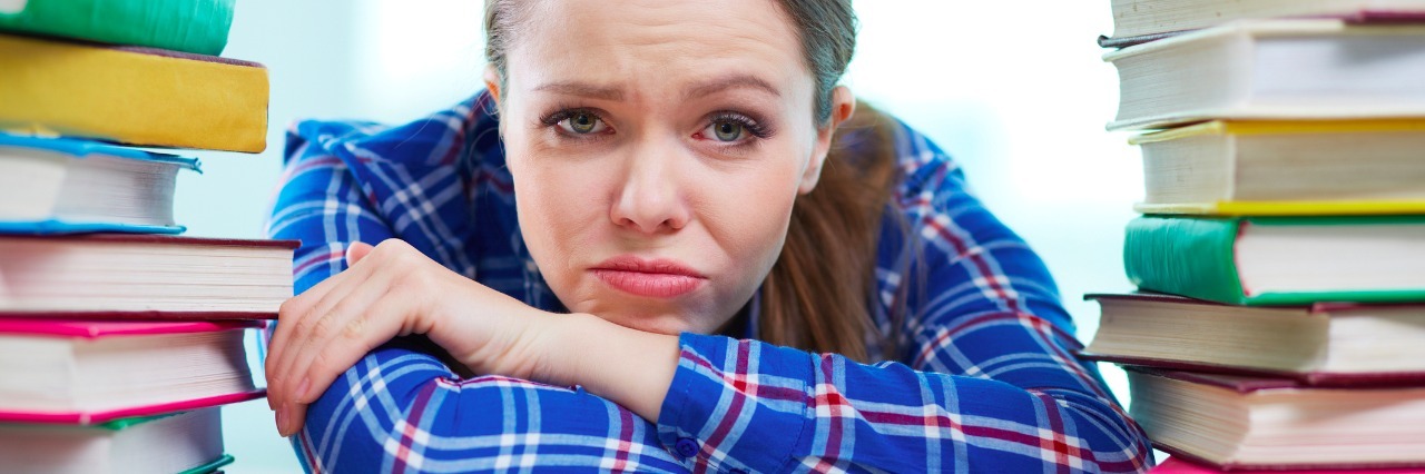 6 Tips for Taking Care of Your Mental Health During Finals A woman looking sad surrounded by books