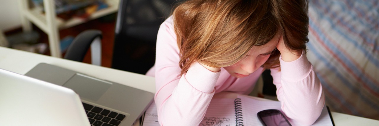 Why I ‘Lashed Out’ as a Child on the Autism Spectrum Girl with hands on head, sitting at desk with laptop, cell phone and notebook