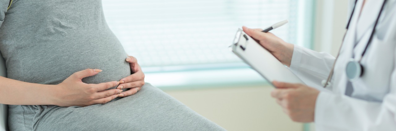 Pregnant woman sits with doctor in doctor's office.