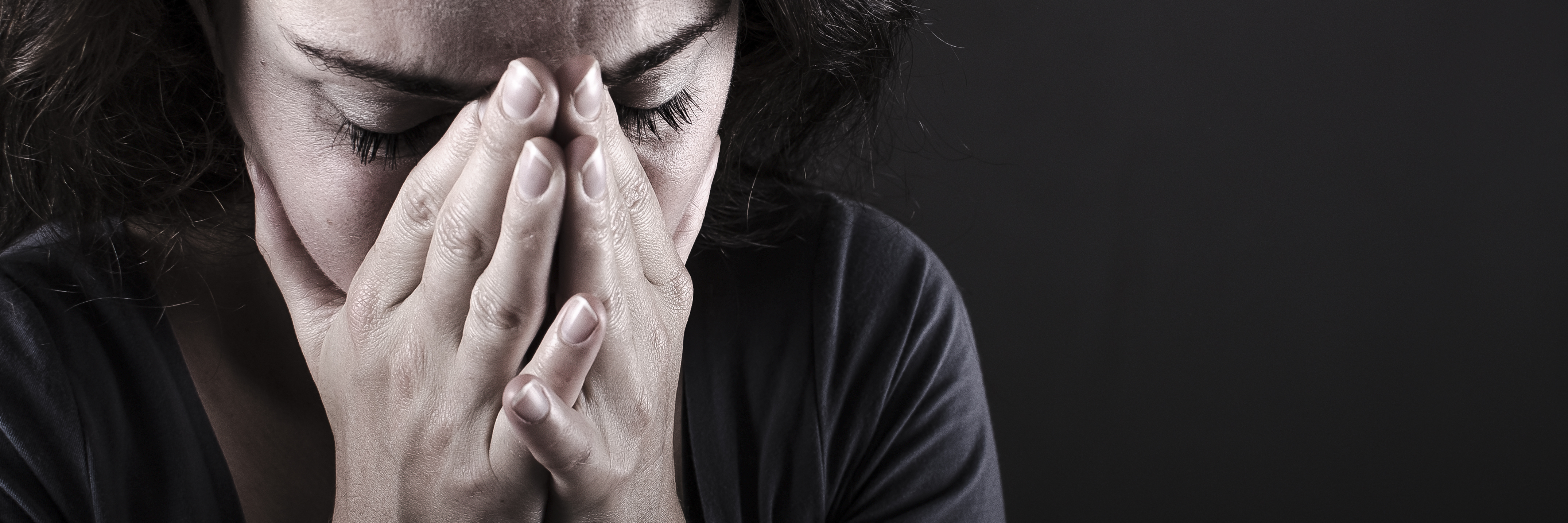 woman on dark background looking scared or depressed with hands covering face