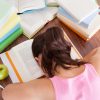 student with her face down in a pile of books on her desk