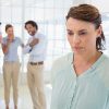 woman looking upset with her coworkers whispering behind her