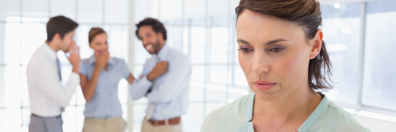 woman looking upset with her coworkers whispering behind her