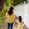 Mother and daughter holding hands, walking down sidewalk