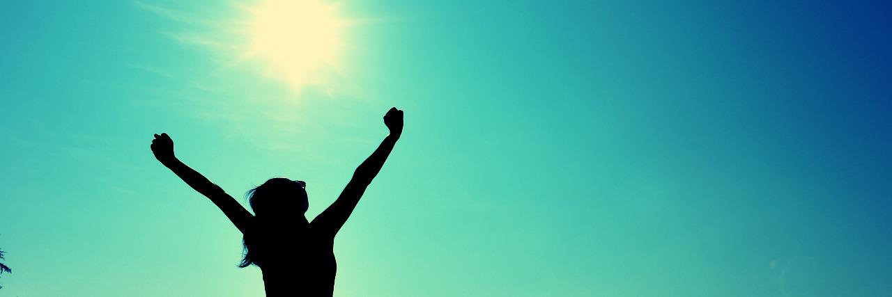 I Stopped Apologizing for My Brain Injury Woman stretching her arms out while standing on a beach.