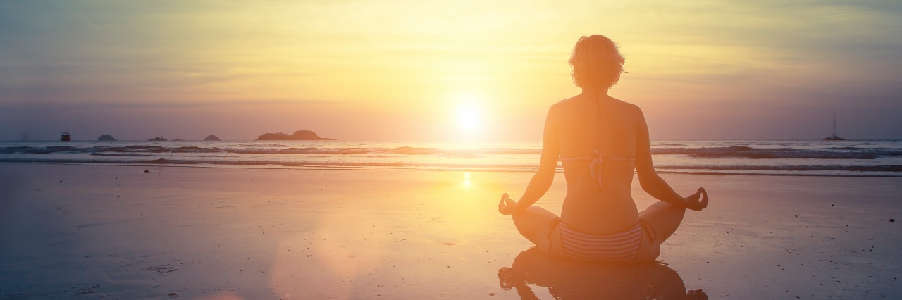 woman meditating on the beach at sunset