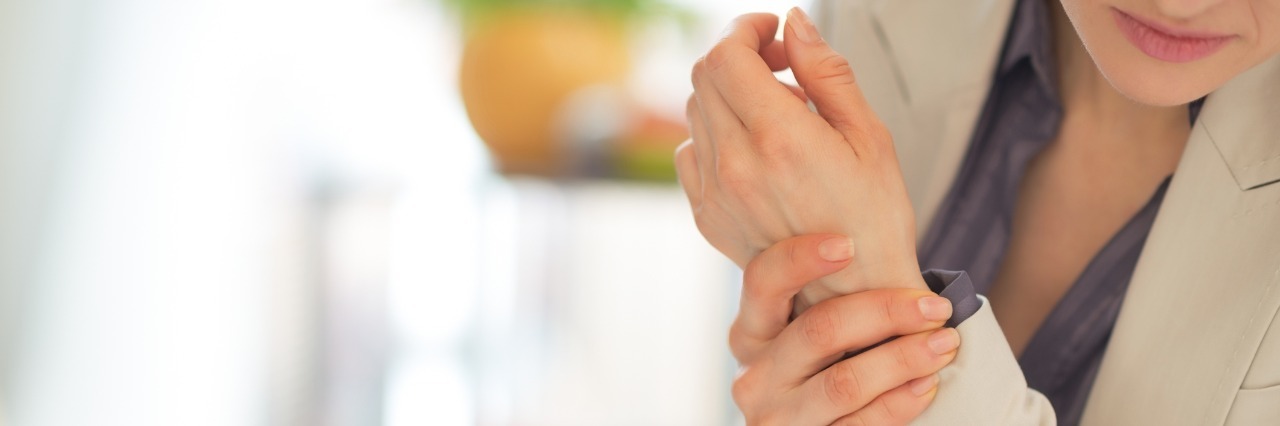 How to Treat Someone With Rheumatoid Arthritis woman sitting at a desk and holding her wrist in pain