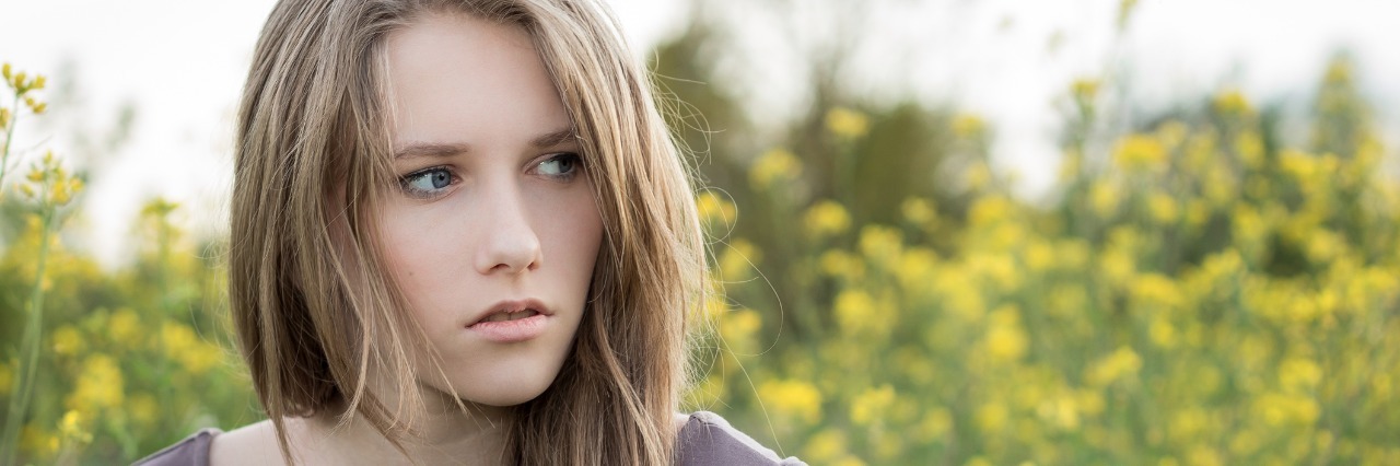How Scoliosis Affects My Life Young woman outside, standing in front of yellow flowers.