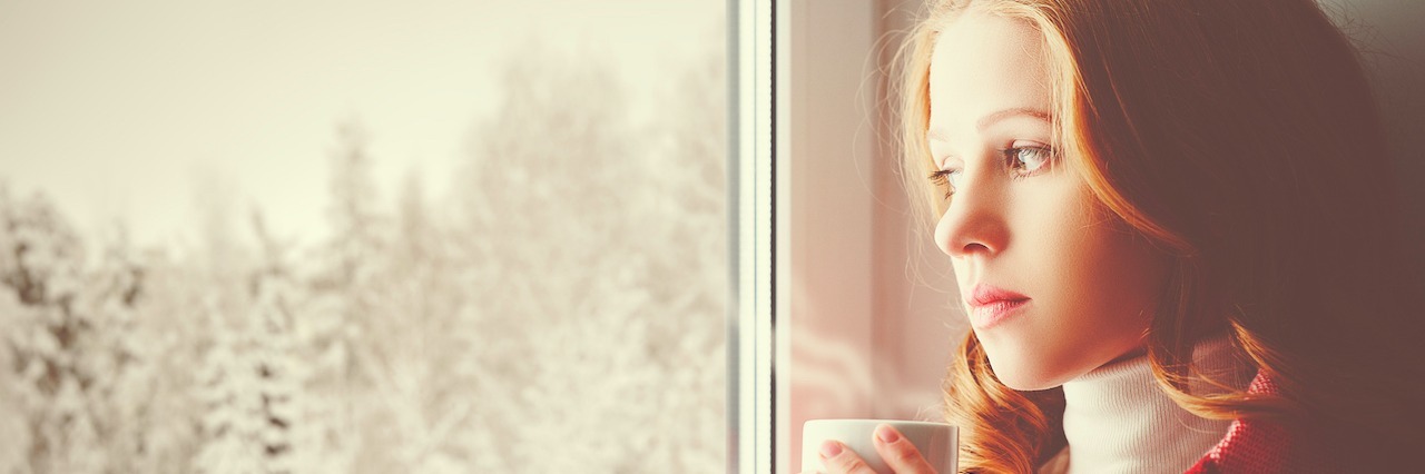 A woman drinking a cup of tea and staring out a window