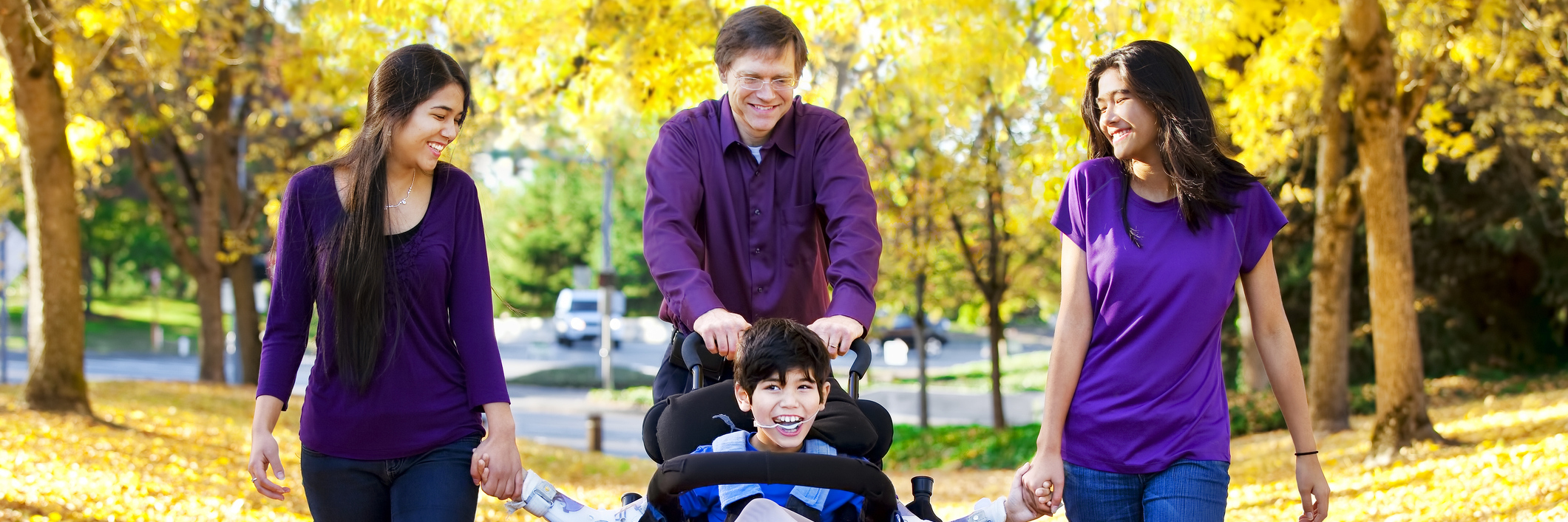 How to Help Families Affected by Disability Family with disabled child in wheelchair walking among autumn leaves.