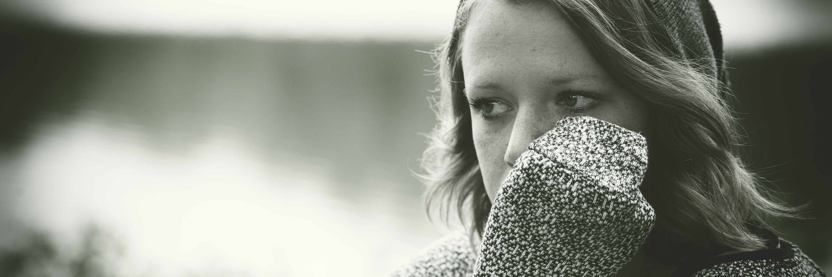 woman sitting outdoors wearing jumper and has arm covering part of her face looking sad
