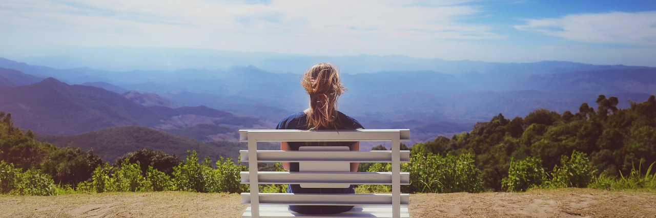 As a Person With a Disability, I Am Never 'Sitting Alone' Young woman sitting on a bench looking at a beautiful sky.
