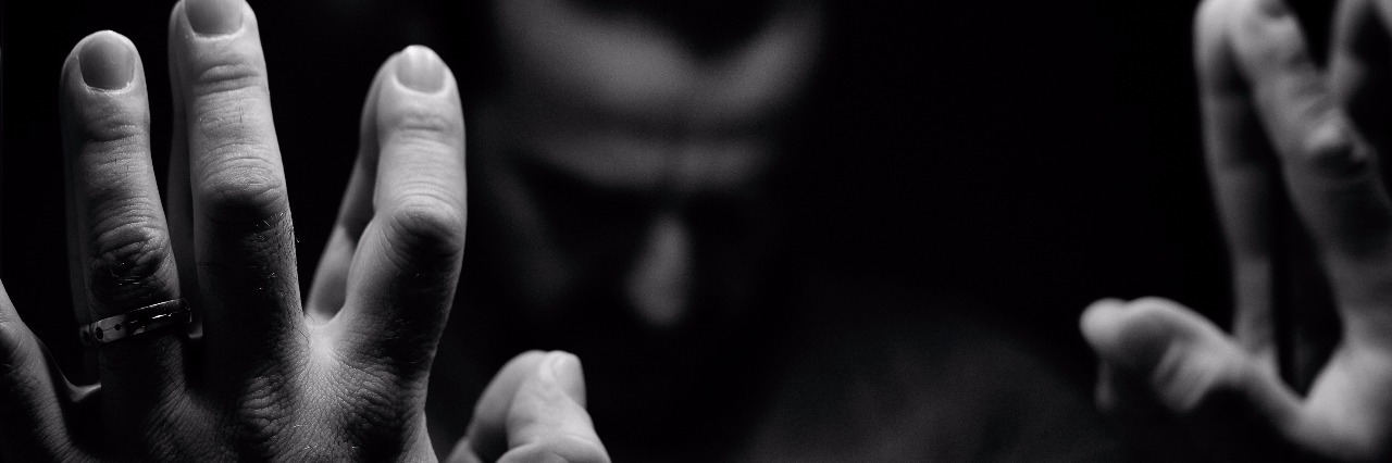 black and white image of man with hands against mirror and head bowed, mostly in darkness