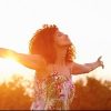 woman standing outside with her arms outstretched and the sun setting behind her