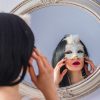 Woman looks in mirror, taking off mask.