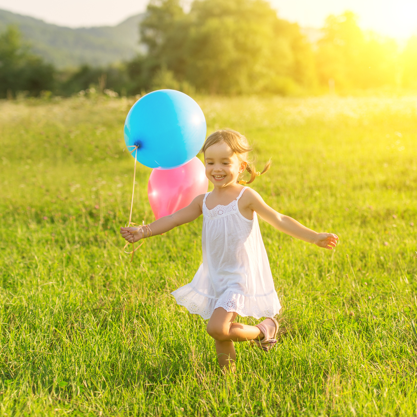 young girl laughing and running through a field with balloons