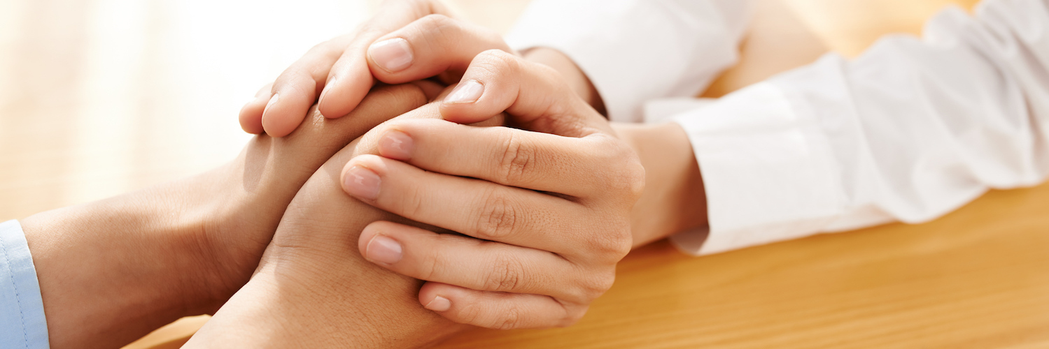 Two people sitting across from each other at a table, one person's hands holding other's in supportive gesture