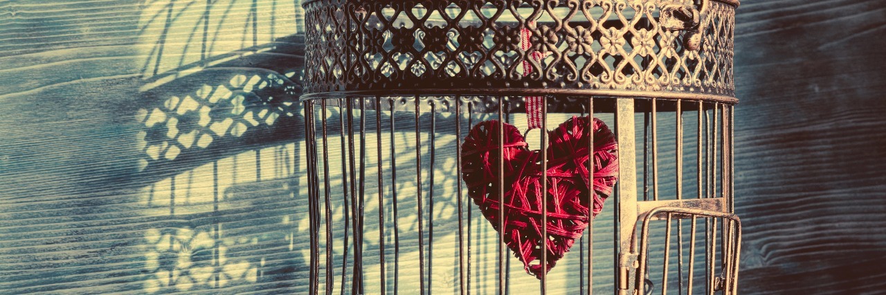 heart trapped inside vintage birdcage with shadows cast on wall