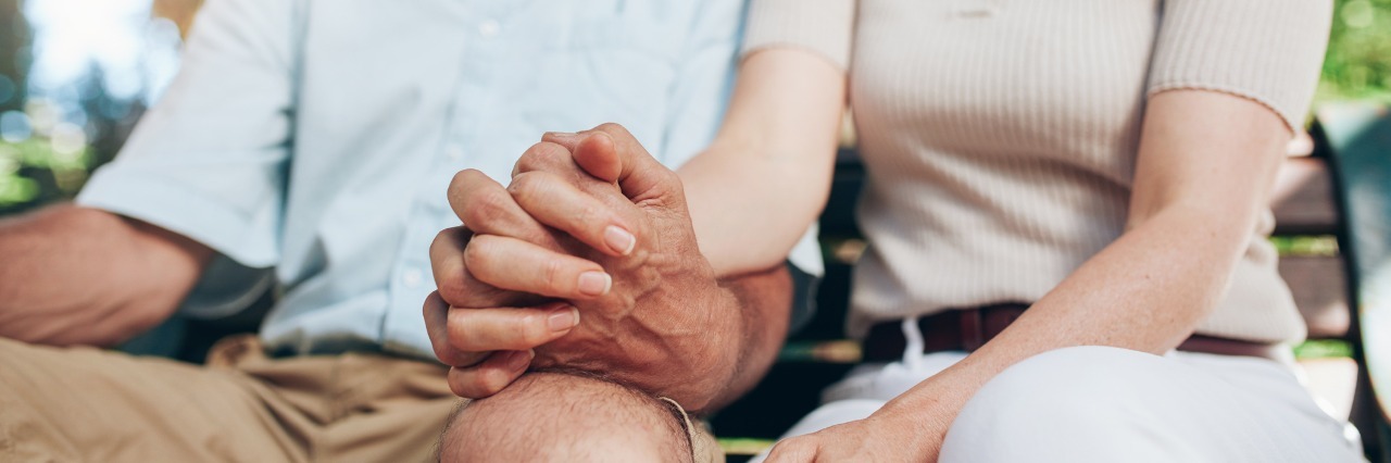 husband and wife holding hands and sitting on park bench