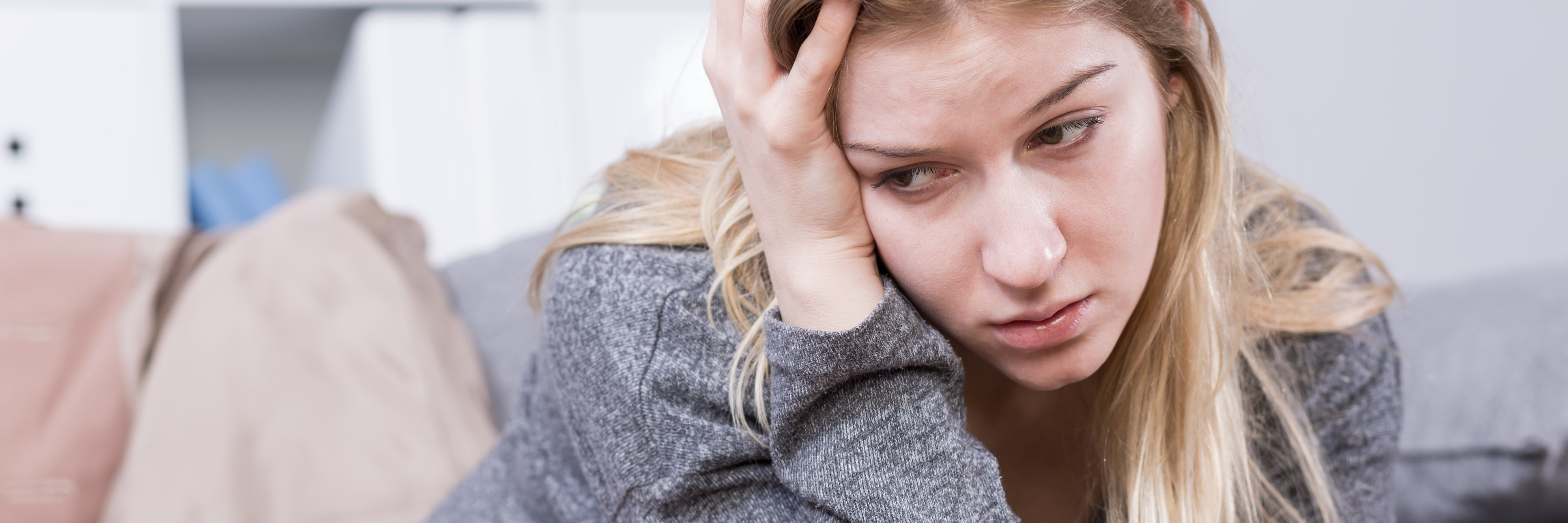 What It's Like Slipping Into Postpartum Depression on Day One new mother with postpartum depression sitting on sofa looking upset with hand in hair