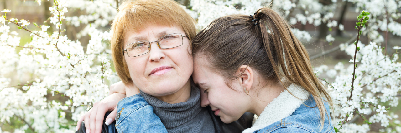 How My Mother Supported Me Through Mental Illness Growing Up Portrait of mother and daughter. Daughter tenderly embraces mother in the orchard.