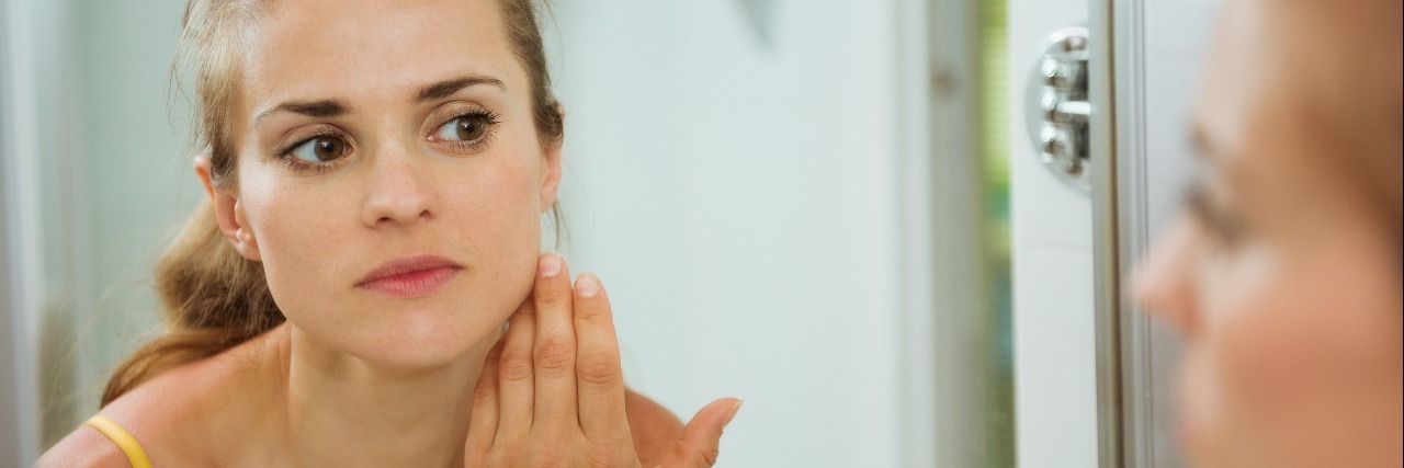 Things People Don't Realize About Body-Focused Repetitive Behavior young woman checking her face in bathroom mirror
